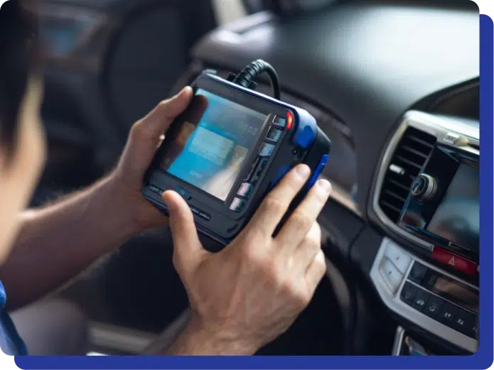 Person holding a diagnostic device inside a car, checking the vehicle's system near the dashboard.