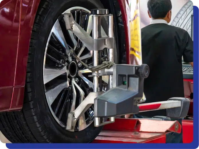 Close-up of a car's wheel and alignment equipment with a mechanic working in the background.