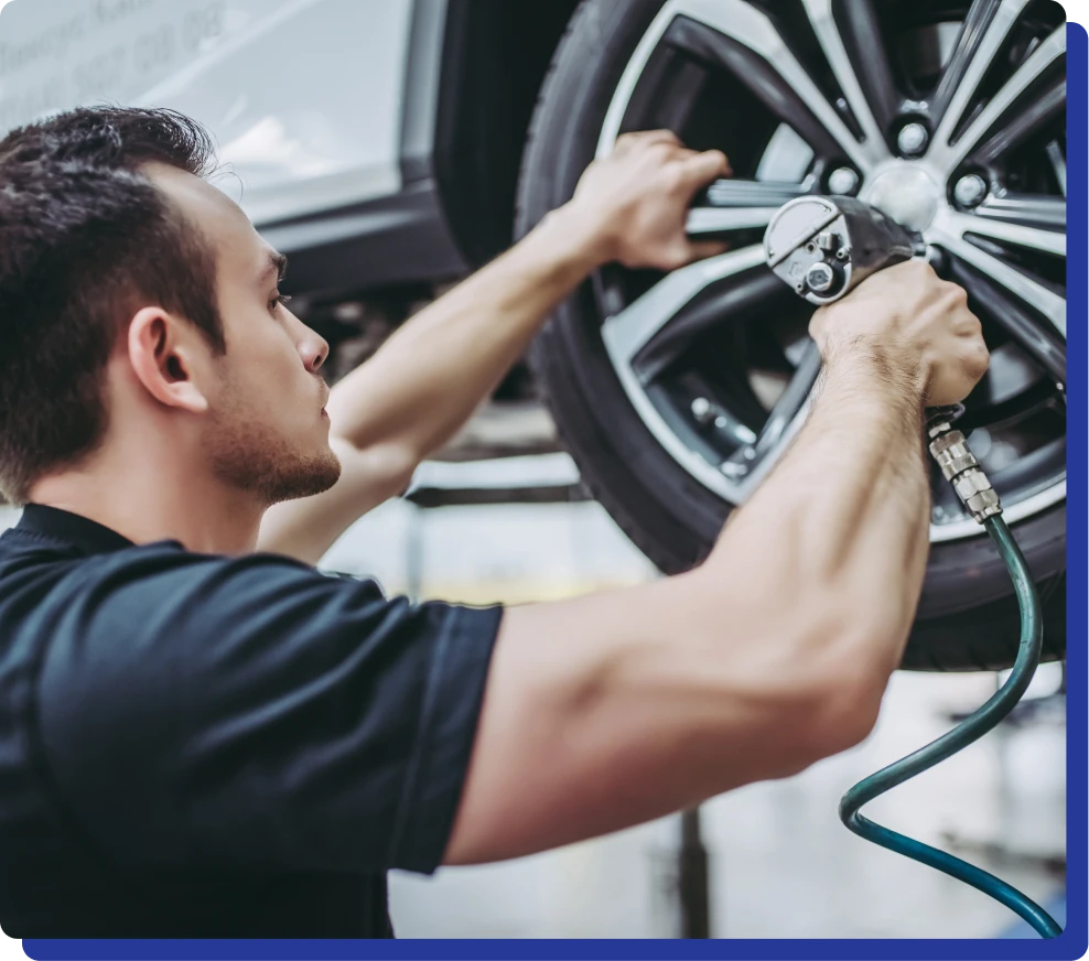 Mechanic using a pneumatic tool to tighten a wheel on a lifted car.