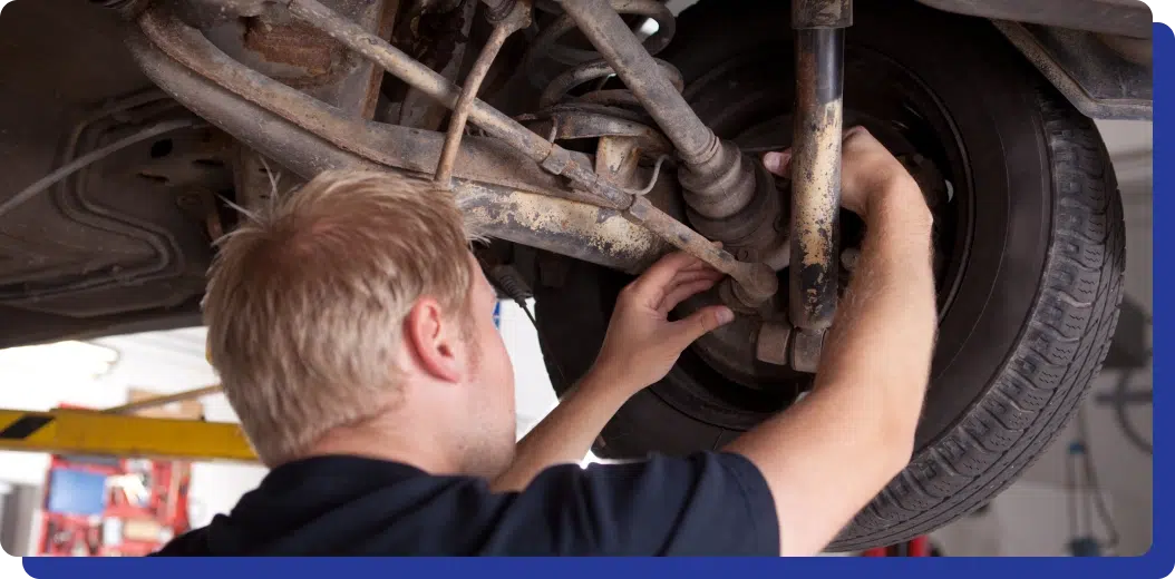 Top Auto Repair in Kodiak, AK with Midtown Auto Repair Services. A mechanic inspects and works on the underside of a vehicle, focusing on the suspension area near the wheel.