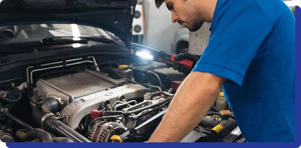 a man holding a flashlight while looking at a car engine