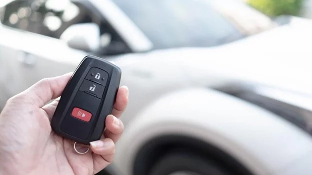 Car key fob services in Kodiak, AK by Midtown Auto Repair Services. Image of a hand holding a car key fob with a white vehicle in the background, illustrating the convenience and security of modern keyless entry systems.