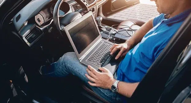 Vehicle Programming and Software Update Service by Midtown Auto Repair Services in Kodiak, AK: Technician sitting inside a car, using a laptop to perform a vehicle software update, illustrating the importance of regular software updates for improved performance, safety, and new features.