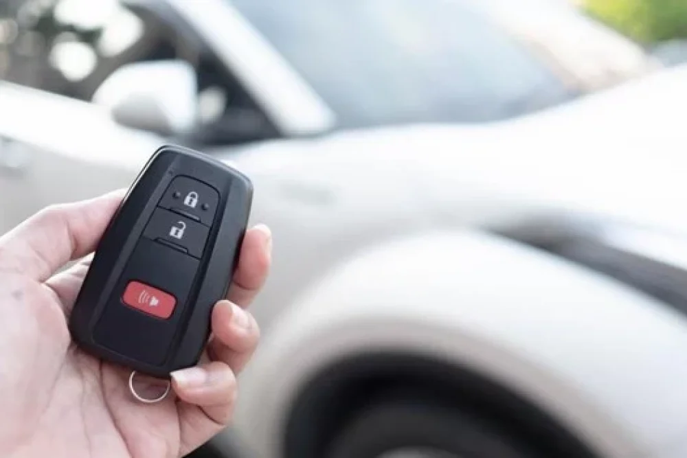 Car key fob services in Kodiak, AK by Midtown Auto Repair Services. Image of a hand holding a car key fob with a white vehicle in the background, illustrating the convenience and security of modern keyless entry systems.